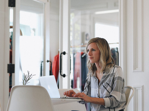 femme blonde assise sur un fauteuil dans sa boutique tape sur son ordinateur