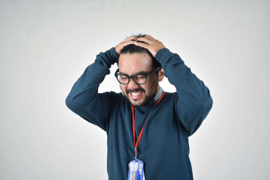 Homme en pull bleu se tient la tête avec les deux mains et grimace
