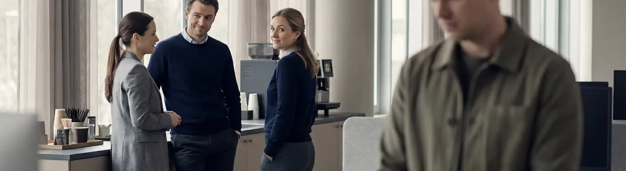 Groupe de collègues échangeant un rire discret tandis qu’un salarié isolé, flou au premier plan, semble mis à l’écart ; illustration de l’humour toxique et des dynamiques relationnelles pouvant précéder un harcèlement moral.