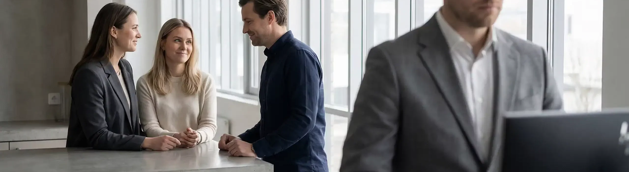 Employé concentré et isolé devant son ordinateur tandis que trois collègues discutent en arrière-plan ; illustration de la surcharge de travail et de l’isolement professionnel.